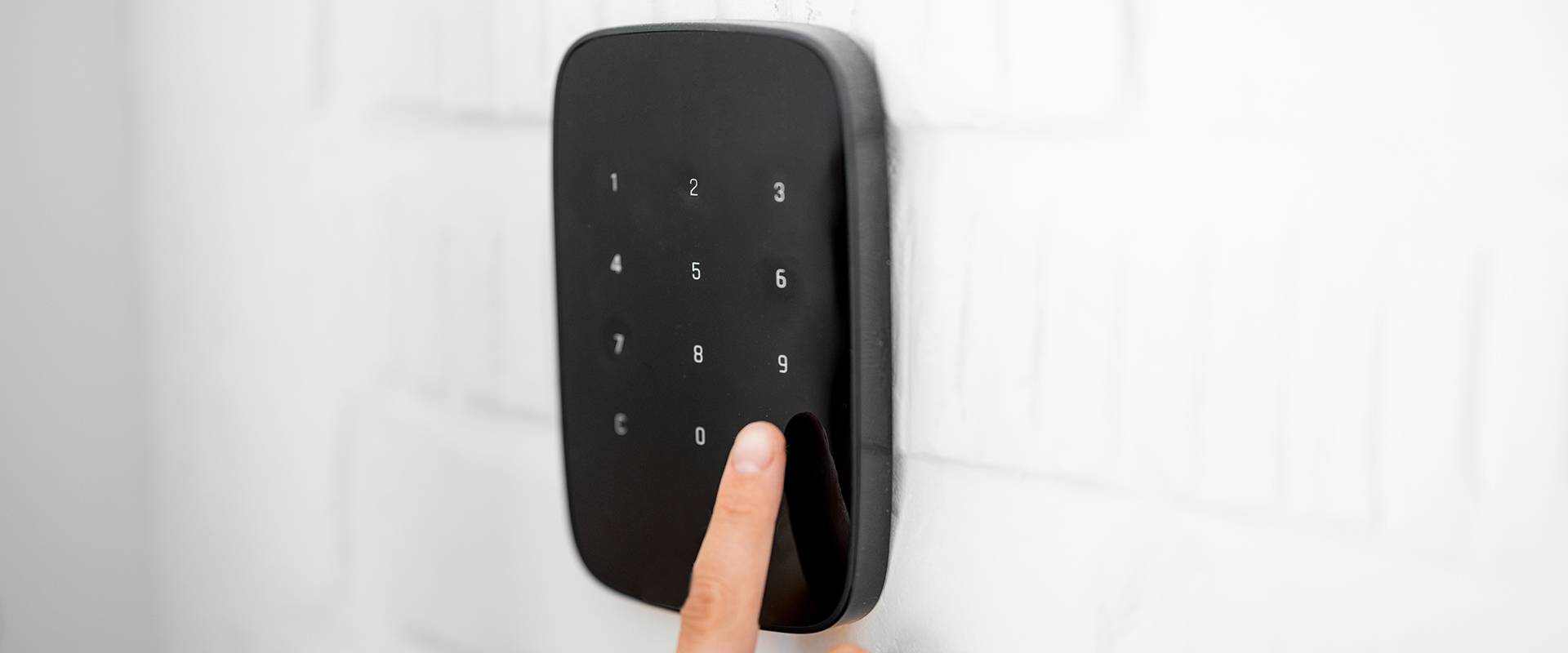 Tastierino di controllo accessi nero con dita che inseriscono codice FGV Impianti Biella S.R.L. Tastierino numerico di colore nero montato su una parete bianca. I pulsanti retroilluminati sono disposti in file ordinate. Un dito umano sta premendo uno dei tasti centrali durante la digitazione di un codice di accesso.
