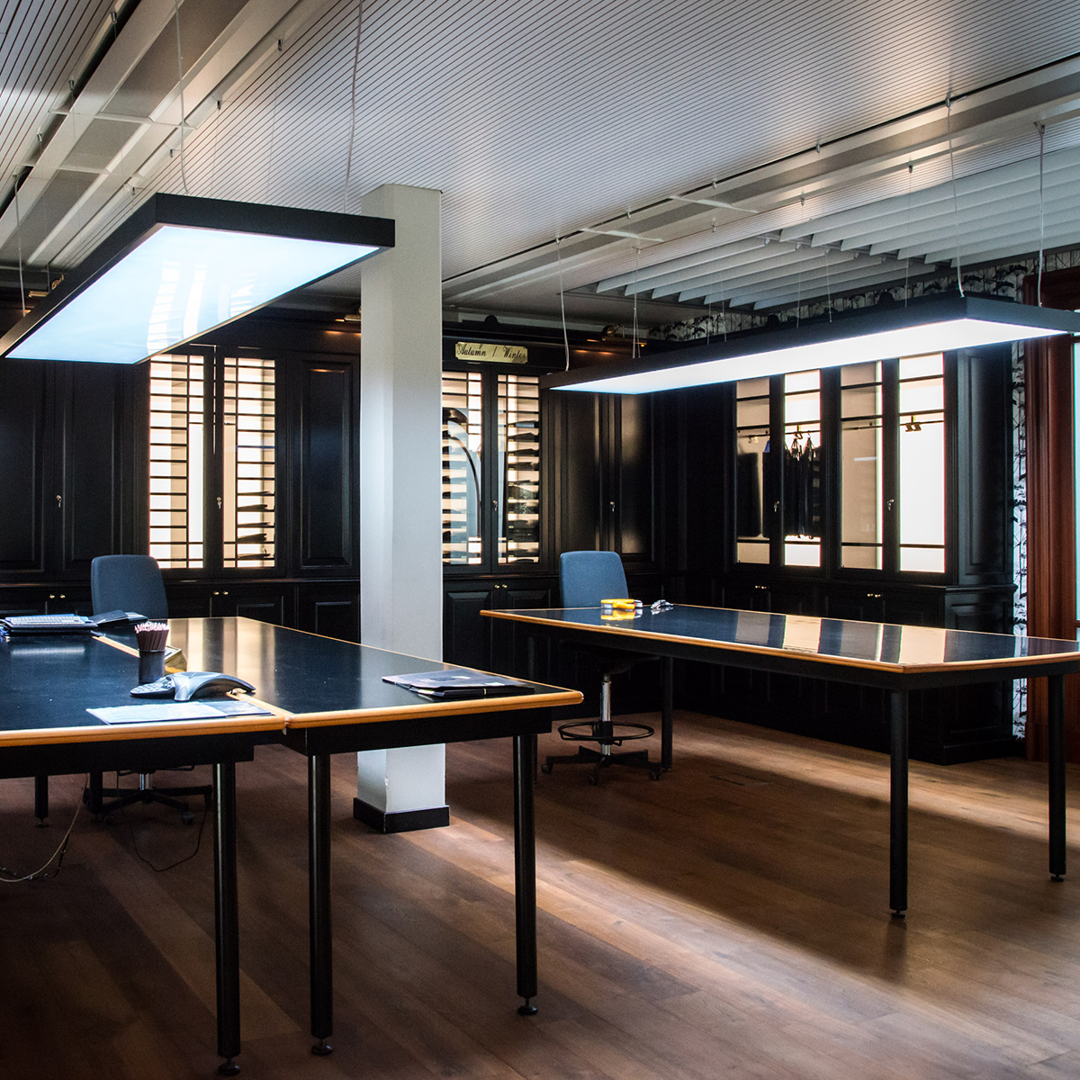 FGV Impianti Biella S.R.L. Ufficio open space con scrivanie, illuminazione moderna e pavimento in legno
Sala ufficio con pavimento in legno e grandi scrivanie scure con bordo di legno,disposte in open space e una colonna bianca al centro. Al soffitto è installato un corpo illuminante sospeso a forma rettangolare. Alle pareti, Grandi armadi retroilluminati di legno scuro con ante di vetro