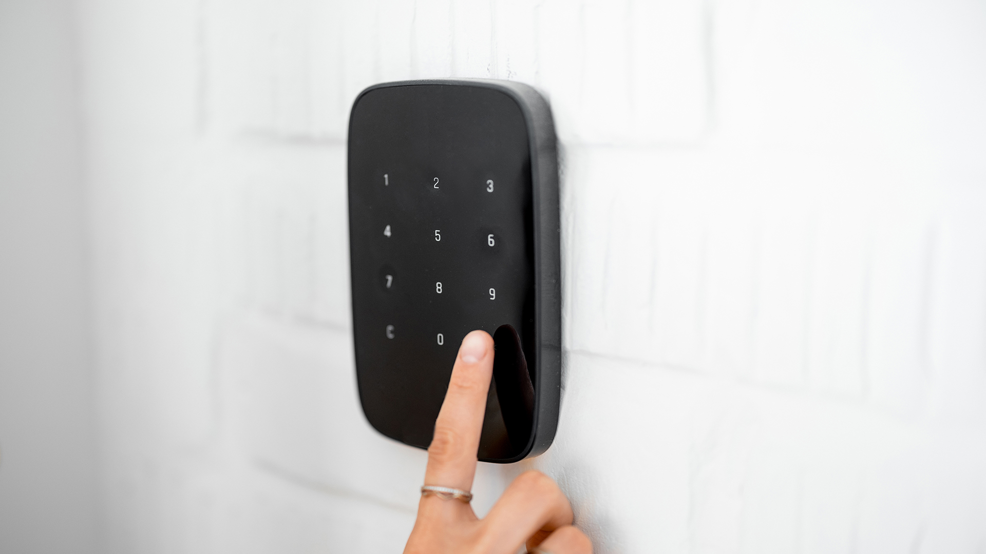 FGV Impianti Biella S.R.L. Tastierino di controllo accessi nero con dita che inseriscono codice Tastierino numerico di colore nero montato su una parete bianca. I pulsanti retroilluminati sono disposti in file ordinate. Un dito umano sta premendo uno dei tasti centrali durante la digitazione di un codice di accesso.