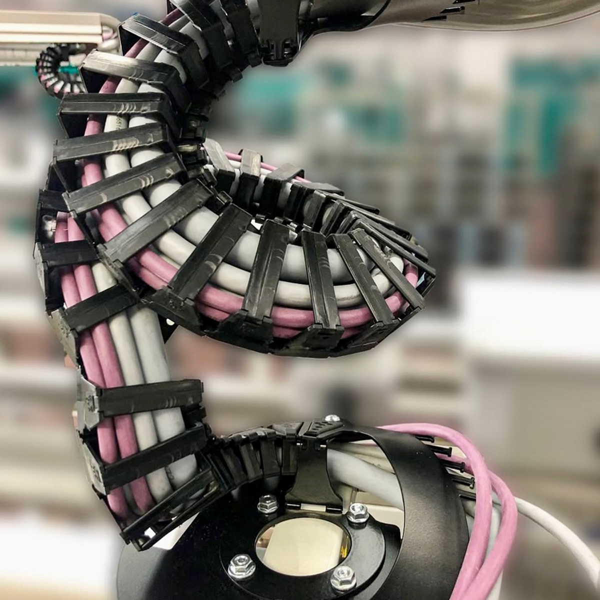 Fgv Impianti Biella Srl Automazioni Braccio robotico industriale con cablaggio elettrico protetto.
Braccio meccanico industriale articolato, con numerosi cavi elettrici avvolti in guaine protettive che seguono i movimenti della struttura. È montato in un ambiente produttivo con elementi metallici e apparecchiature di automazione visibili sullo sfondo.