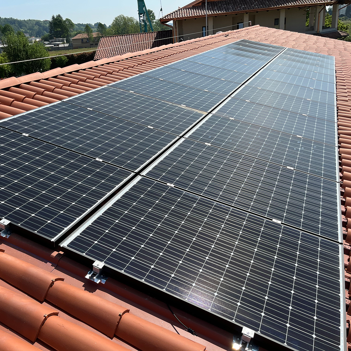 Fgv Impianti Biella Srl Fotovoltaico Pannelli solari installati su tetto in tegole rosse
Pannelli fotovoltaici neri installati in più file su un tetto rivestito da tegole rosse. Il cielo azzurro illumina l’impianto dall’alto e sul bordo superiore del tetto si intravedono alberi verdi e altre case