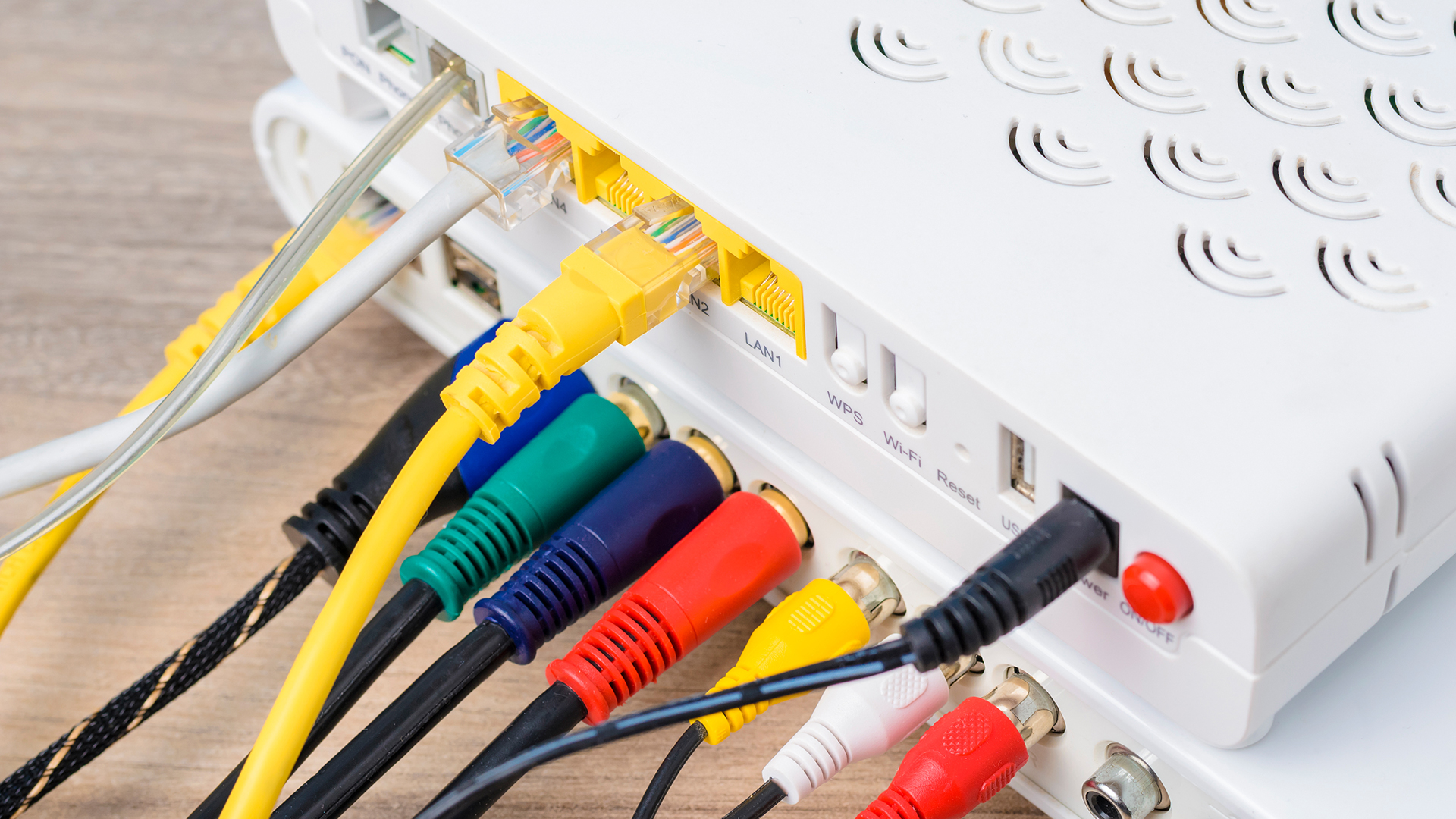 FGV Impianti Biella S.R.L. Modem router bianco con prese collegate da cavi Ethernet e RCA Modem router bianco appoggiato su un piano in legno chiaro. Sul retro sono collegati cavi Ethernet gialli, connettori RCA rosso, bianco e giallo, oltre a un cavo coassiale nero. I cavi si estendono in più direzioni, occupando tutte le prese visibili.