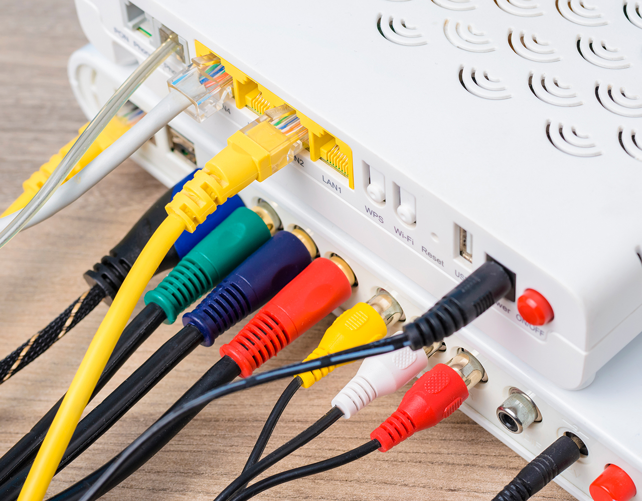 FGV Impianti Biella S.R.L. Modem router bianco con prese collegate da cavi Ethernet e RCA
Modem router bianco appoggiato su un piano in legno chiaro. Sul retro sono collegati cavi Ethernet gialli, connettori RCA rosso, bianco e giallo, oltre a un cavo coassiale nero. I cavi si estendono in più direzioni, occupando tutte le prese visibili.