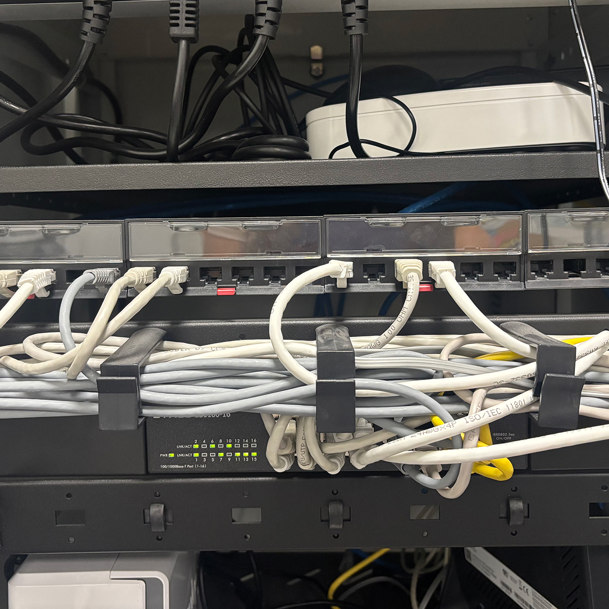 FGV Impianti Biella S.R.L. Reti Tv Lan antenne tv Armadio rack tecnico con cablaggi ordinati, dispositivi di rete e etichette arancioni Armadio rack professionale a parete, con porte aperte che mostrano una complessa organizzazione di cablaggi elettrici e di rete. All’interno si distinguono patch panel, switch, modem e dispositivi di alimentazione ordinatamente disposti su più livelli. I cavi ethernet sono raggruppati e fascettati in modo ordinato, con etichette arancioni applicate ai singoli connettori per l’identificazione dei circuiti. Sono presenti indicatori LED accesi che segnalano attività e connessione.